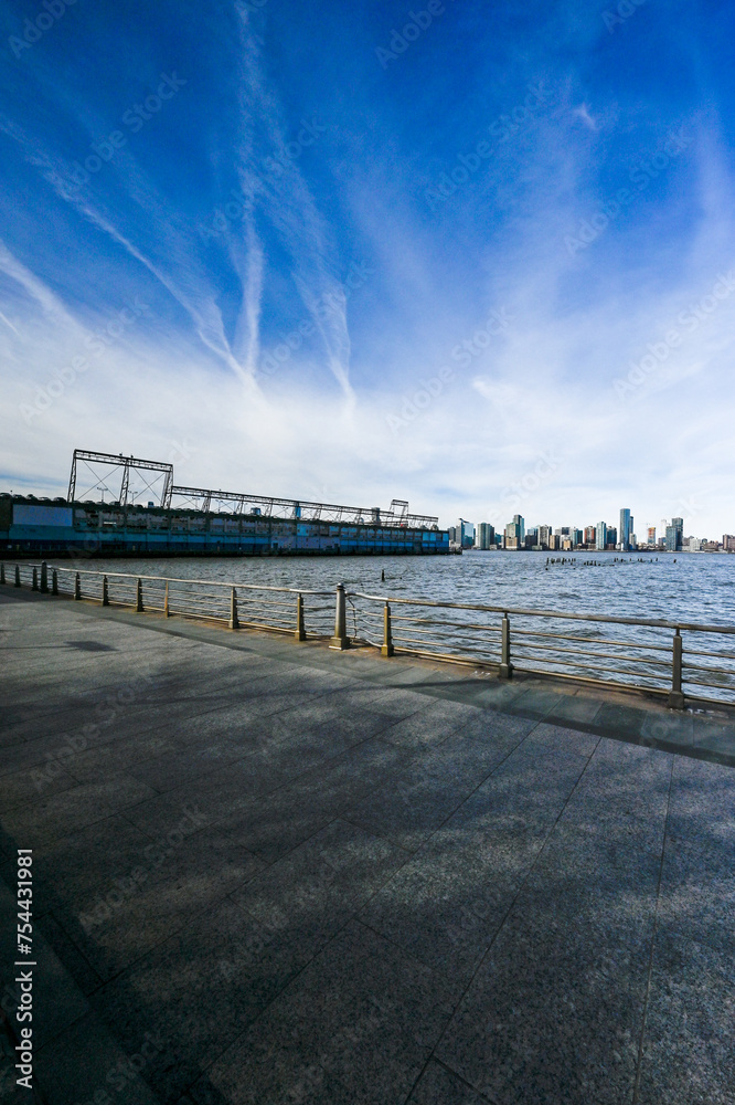 Empty waterfront promenade offering a peaceful view towards the modern skyline, situated along the Hudson River Greenway.