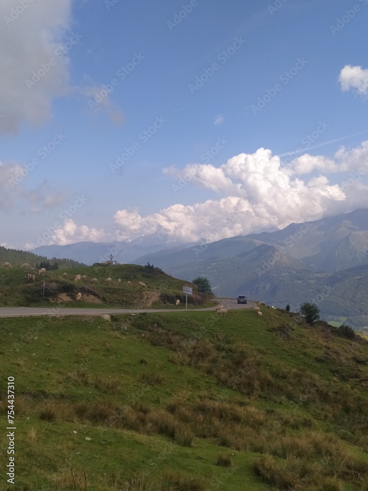 Scenic Mountain Drive: Curvy Road in the Pyrenees with Sheep Grazing Alongside, Beneath a Blue Sky and Fluffy White Clouds