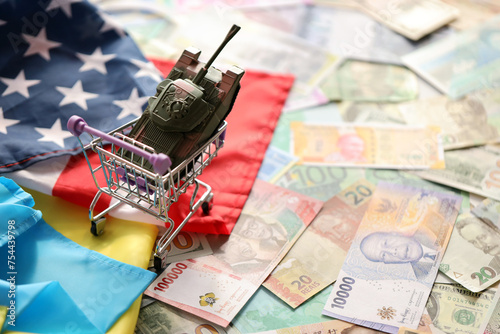 Toy tank on US flag and ukrainian flag on many banknotes of different currency. Background of war funding and military support between United States and Ukraine photo