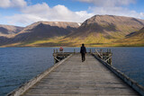 Girl walking on Önundarfjörður Pier and looking at beautiful view over fjord and mountains in Westfjords, Iceland