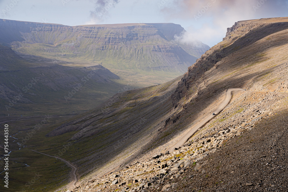 Winding gravel road leading from Bolafjall mountain to Bolungarvík town in Westfjords, Iceland