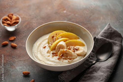 Sweet milky semolina porridge with apples bananas and almonds in a bowl on the table. Healthy children's breakfast.