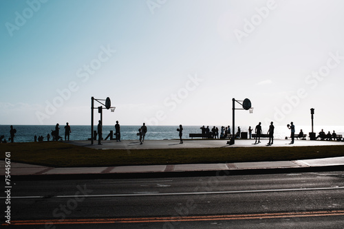 silhouette beach goers playing basketball and strolling 