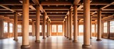 An empty room illuminated by natural light streaming in through large windows, with wooden architectural columns adding structure and elegance. The space is devoid of any people,