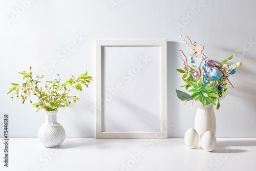 Mockup with a white frame and spring flowers in a vase, easter eggs on a light background. Empty poster frame mockup for presentation design, text, lettering
