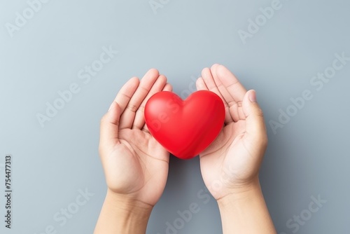 Two hands carefully holding a red heart, symbolizing love, care, and health.