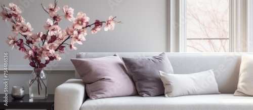 A soft gray couch with cushions is positioned near a window in a modern living room. A vase of flowers adds a touch of nature to the space, which also features a TV.