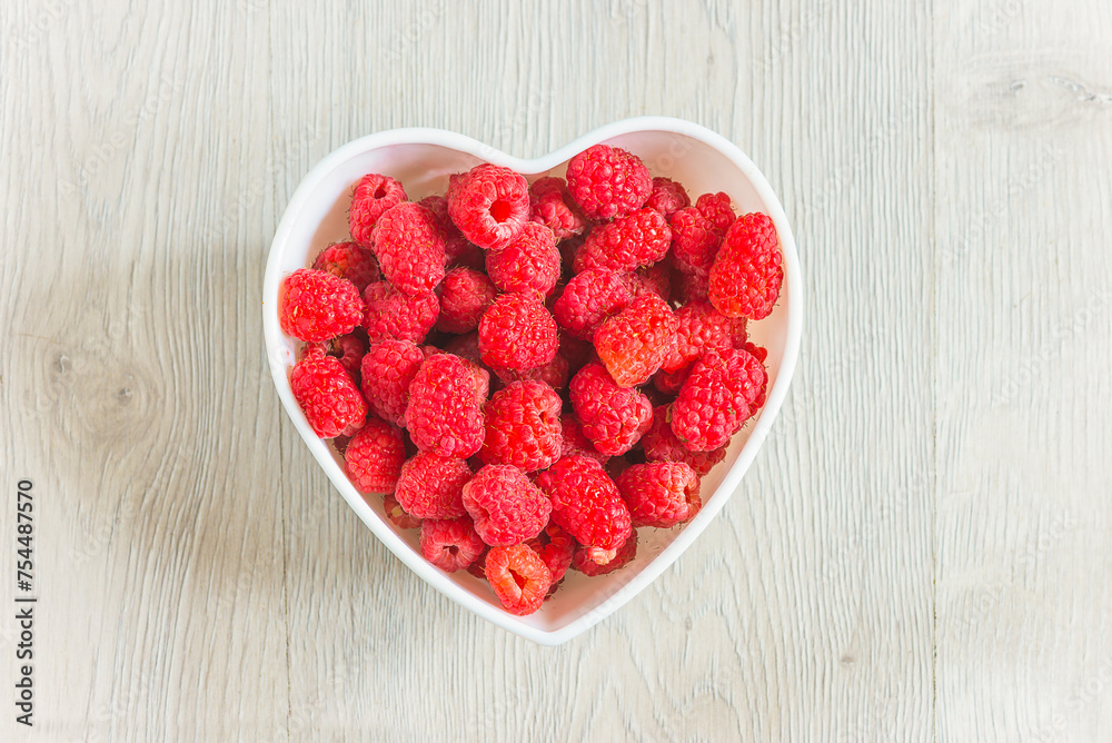 White bowl with red ripe raspberries on a white wooden background White bowl with red ripe raspberries on a white wooden background