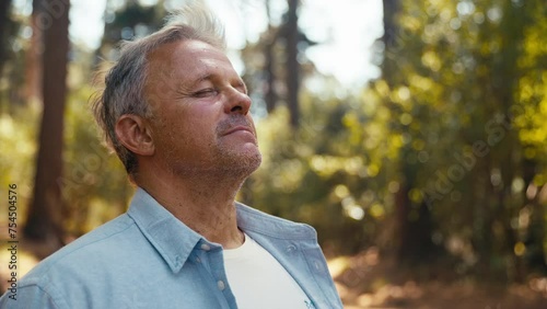 Peaceful senior retired man relaxing standing amongst nature in forest surrounded by trees with closed eyes breathing deeply - shot in slow motion