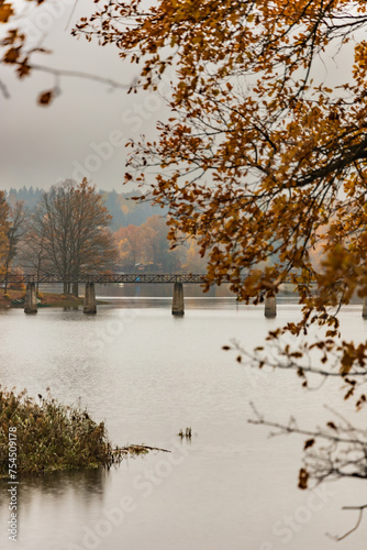 Beautiful view to big lake with small islands full of bushes and long wood and steel bridge at the center seen from small hill at cloudy and rainy morning (ID: 754509178)