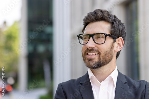 Close-up portrait of a young businessman in an apron and a suit standing outside an office center and looking away with a smile