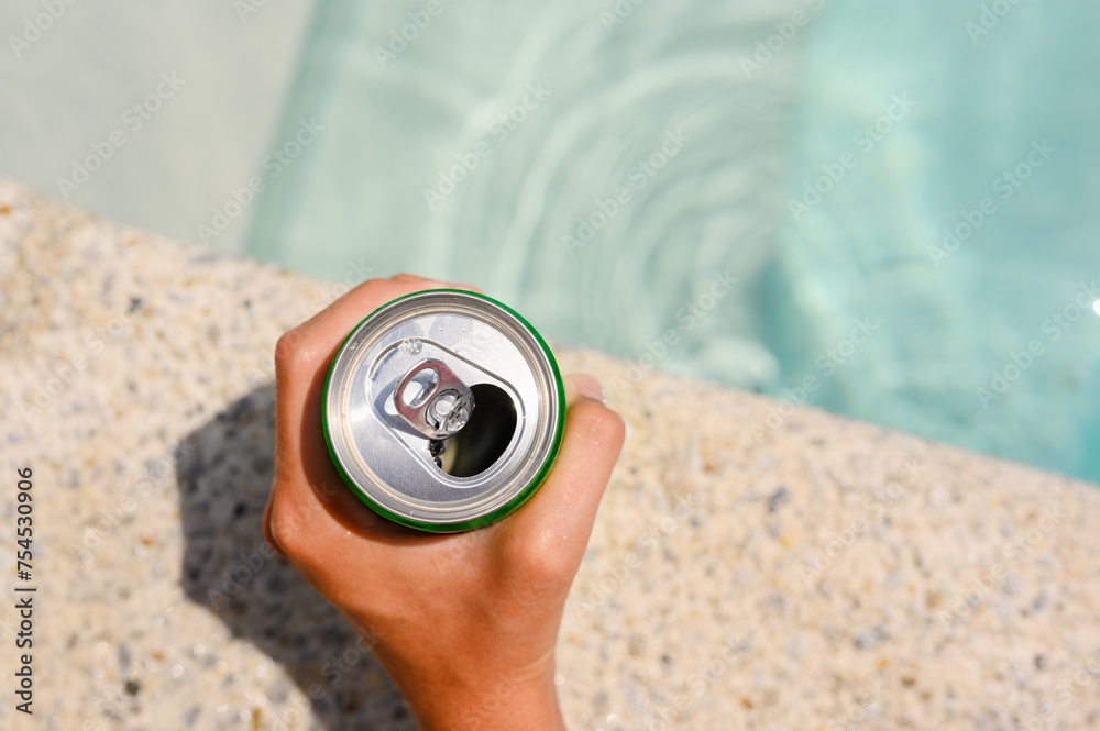 An open can of drink in hand by the pool. Close-up of a drink in hand. Selective Focus An open can of drink in hand by the pool. Close-up of a drink in hand. Selective Focus
