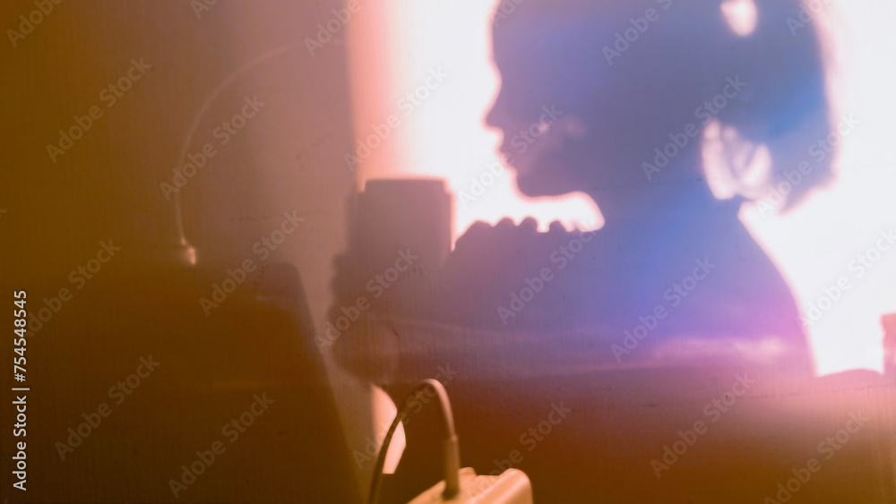 Fototapeta premium Shadow of girl drinking coffee from mug on sunny day. Silhouette of female person in the morning. Woman with thermos cup at home. Film grain texture. Soft focus. Blur