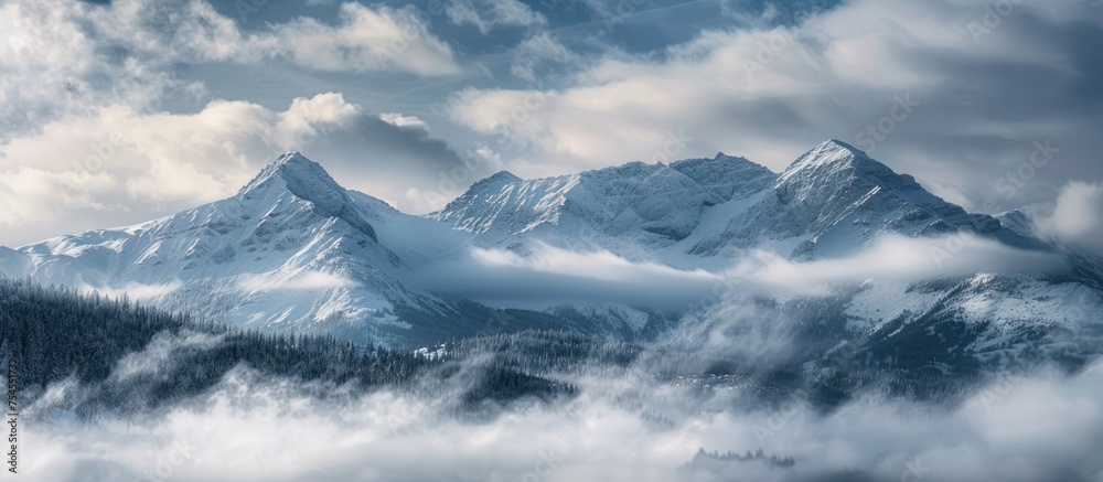 The rugged mountain range stands tall, covered in a blanket of snow and surrounded by dense clouds.
