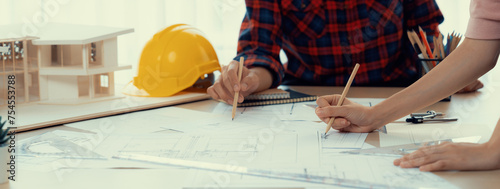 Cropped image of cooperative architect team decide and work together on meeting table with house model, safety helmet and architectural plan scatter around. Closeup. Focus on hand. Burgeoning.