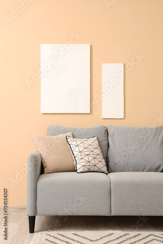 Stylish grey sofa with pillows and paintings near beige wall