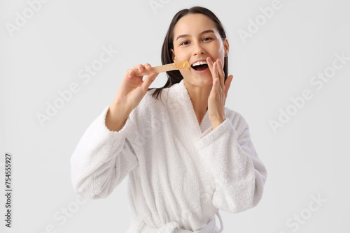 Beautiful young happy woman in bathrobe holding spatula with sugaring paste on grey background
