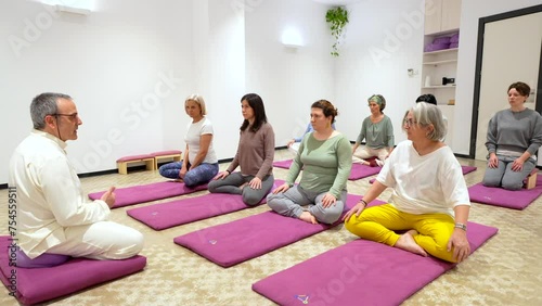 Mature man leading a yoga class full of women doing a lotus position photo