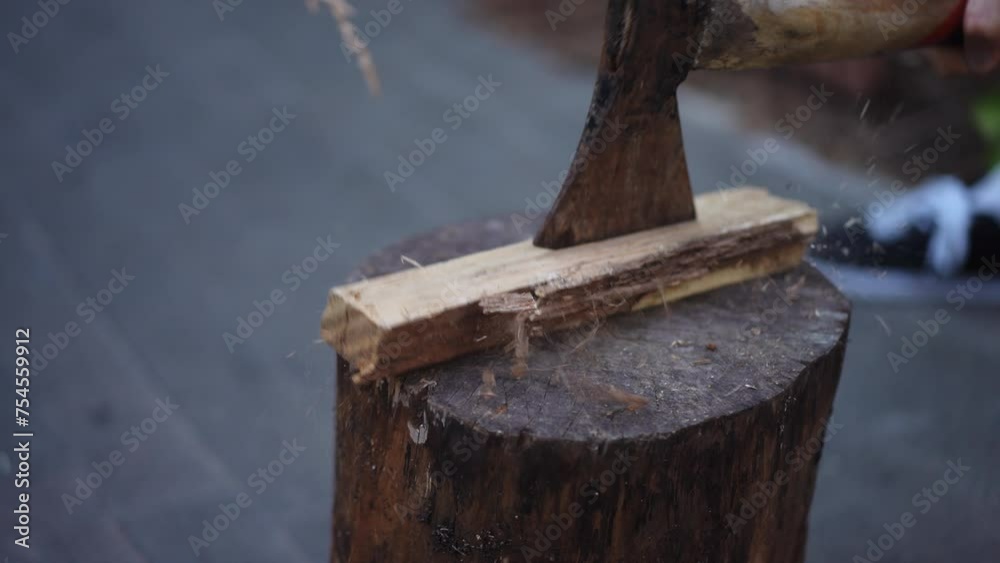 Close-up. A man is trying to cut a piece of wood lying on a log with an axe while standing outdoors. Chopping wood for a fire. Chopping a wood with an ax that lying on a log. Preparation of firewood Close-up. A man is trying to cut a piece of wood lying on a log with an axe while standing outdoors. Chopping wood for a fire. Chopping a wood with an ax that lying on a log. Preparation of firewood