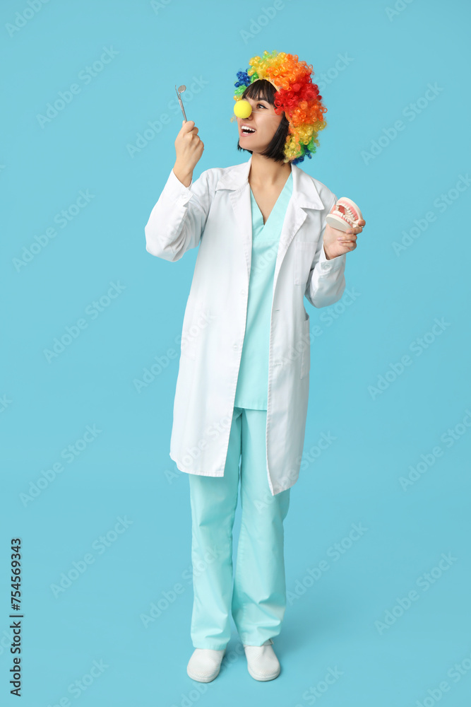 Young smiling female dentist with jaw model on blue background. Fool's day