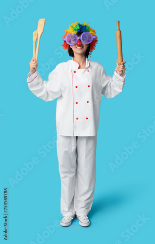 Funny young female chef with kitchen utensils on blue background. Fool's day