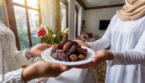 Concept Giving or Charity during Ramadhan Holy Month, Female Muslim Hand Over A Plate of Dates Fruit hurma to Other. Ifthar and Ramadan Kareem Concepts.