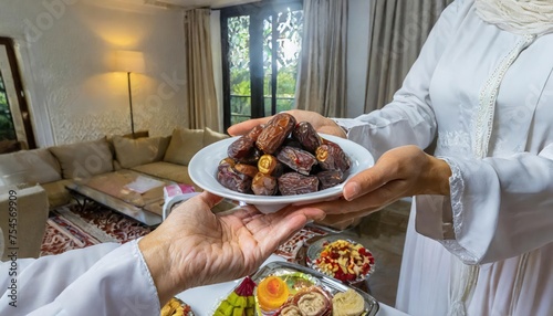 Concept Giving or Charity during Ramadhan Holy Month, Female Muslim Hand Over A Plate of Dates Fruit hurma to Other. Ifthar and Ramadan Kareem Concepts.