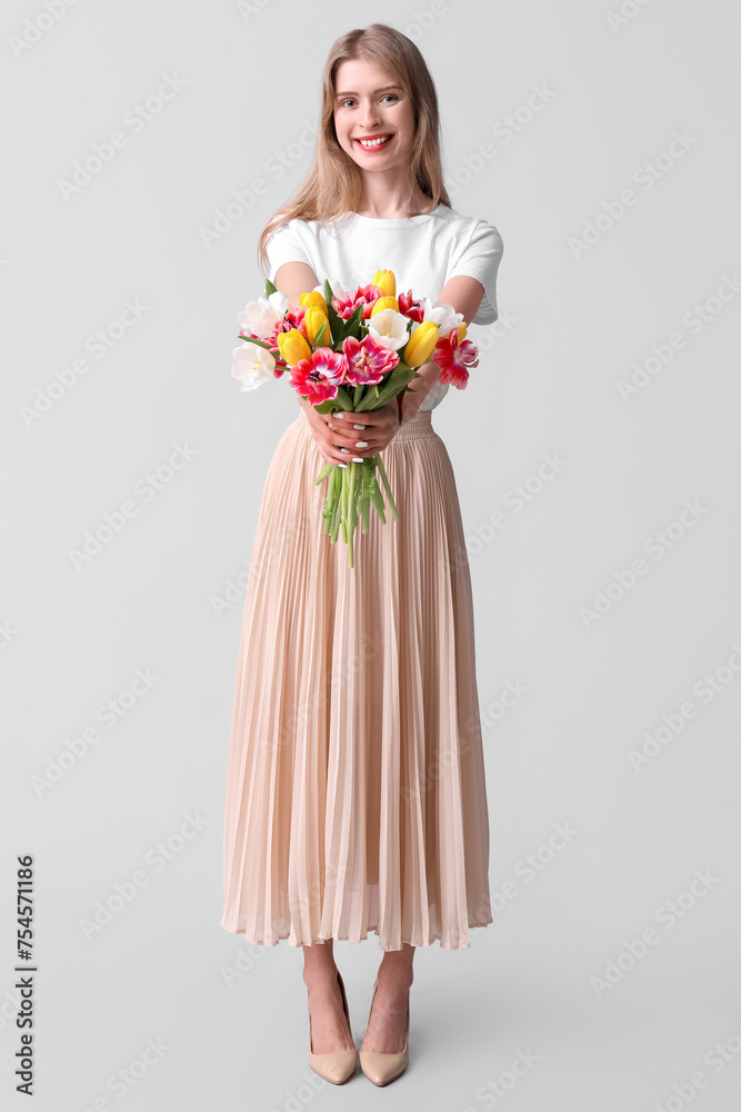 Pretty young woman with bouquet of beautiful tulips on grey background