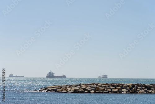 Seascape with a stone pier and lonely ships on the distant horizon on a sunny day