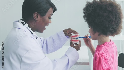 Female dentist explains how to brush teeth properly to girl in clinic photo