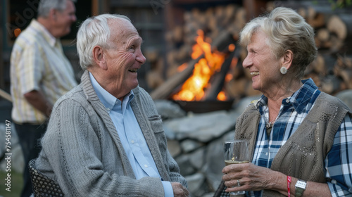 An elderly man and woman share a joyful chat and smiles, standing by a blazing fire pit during an evening gathering photo