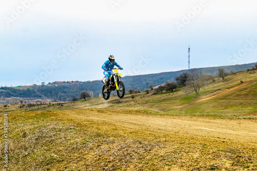 Fototapeta Naklejka Na Ścianę i Meble -  A person on a dirt bike with helmet rides through a dirt road under the sky