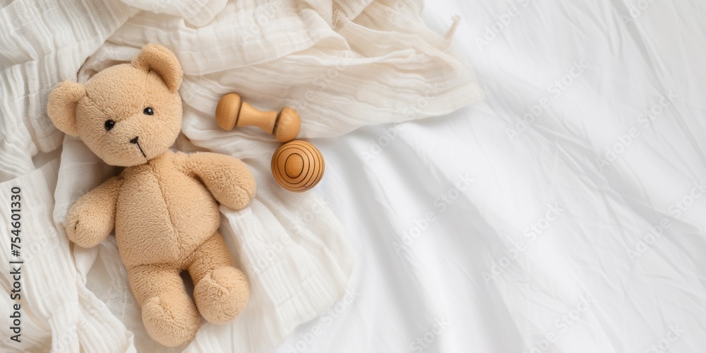 Soft beige teddy bear alongside a wooden rattle toy, laid out on a white blanket with gauzy fabric, symbolizing innocent and classic childhood comfort.