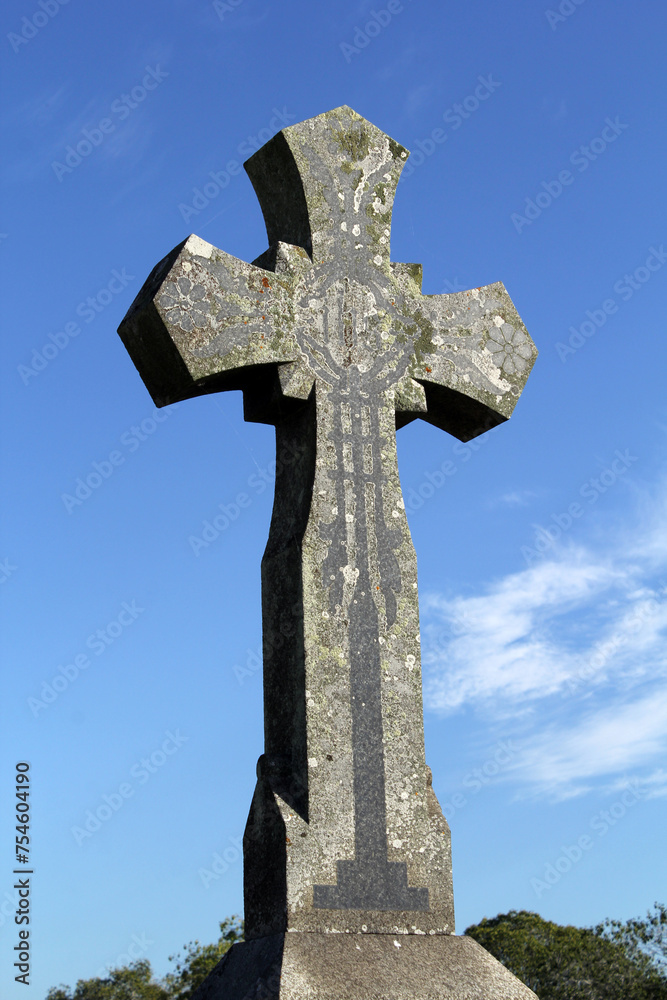 Cross on a headstone against a blue sky with clouds