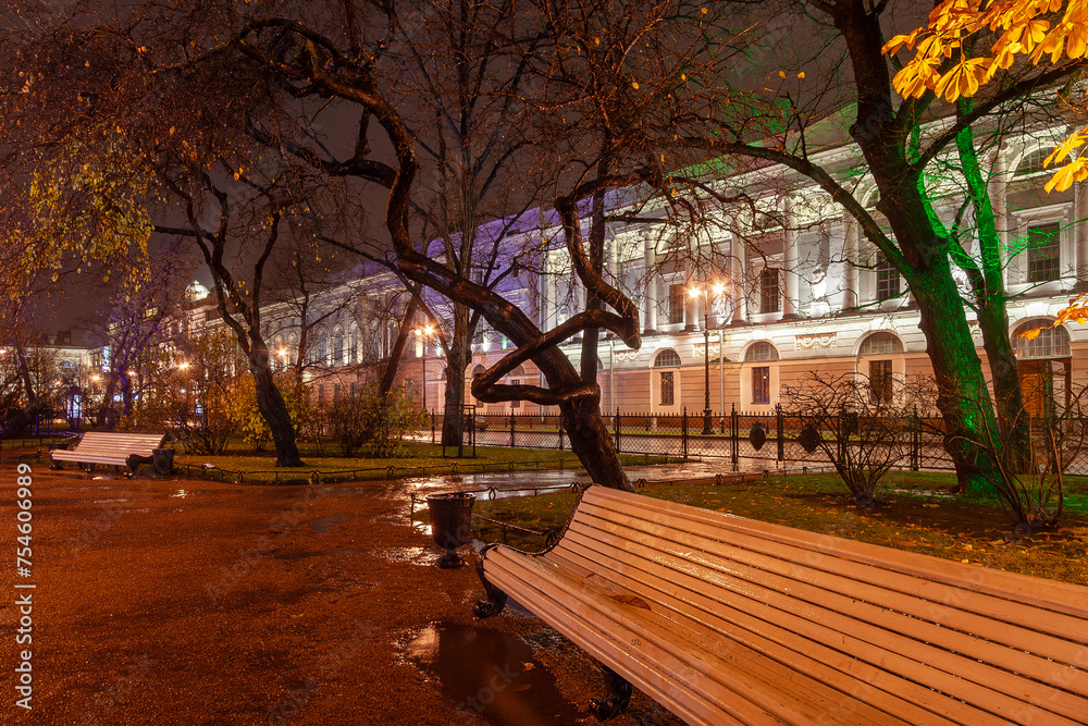 Evening view of empty benches in a city park during the rain. Catherine Garden, Historical Center of St. Petersburg, Russia. Night city. Rainy autumn weather.