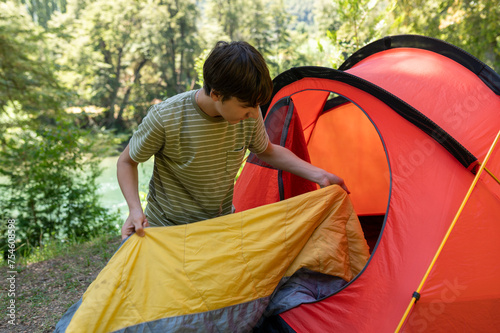 Happy teenager preparing camp and storing his sleeping bag in the tent before going out to enjoy the landscape during his summer vacation in Patagonia. photo