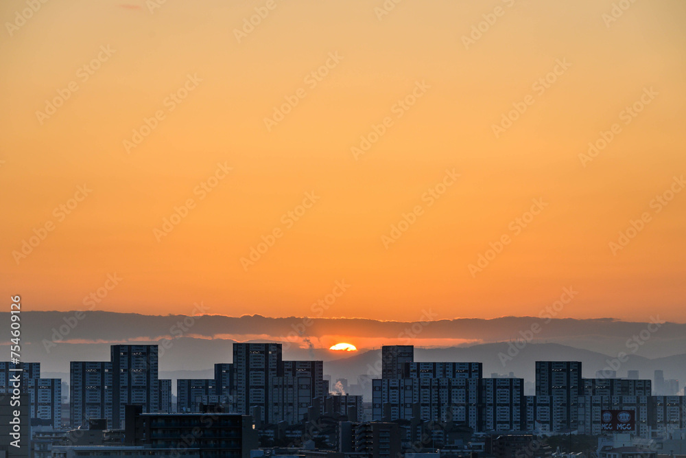 Fototapeta premium 都市の夜明け。神戸市から芦屋大阪方面をのぞむ。生駒の山並みから朝日が昇る。都市のビルがシルエットで浮かぶ。