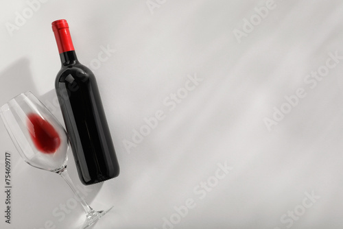 Bottle of expensive red wine and wineglass on light grey background, top view. Space for text