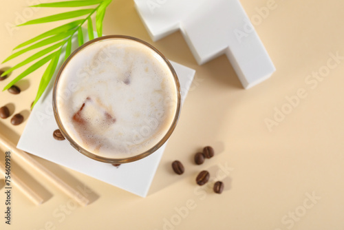 Refreshing iced coffee with milk in glass and beans on pale yellow table  top view. Space for text