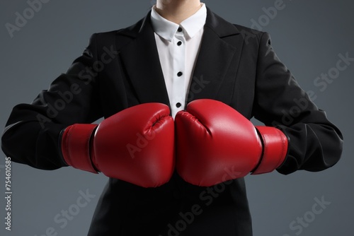 Businesswoman in suit wearing boxing gloves on grey background, closeup © New Africa