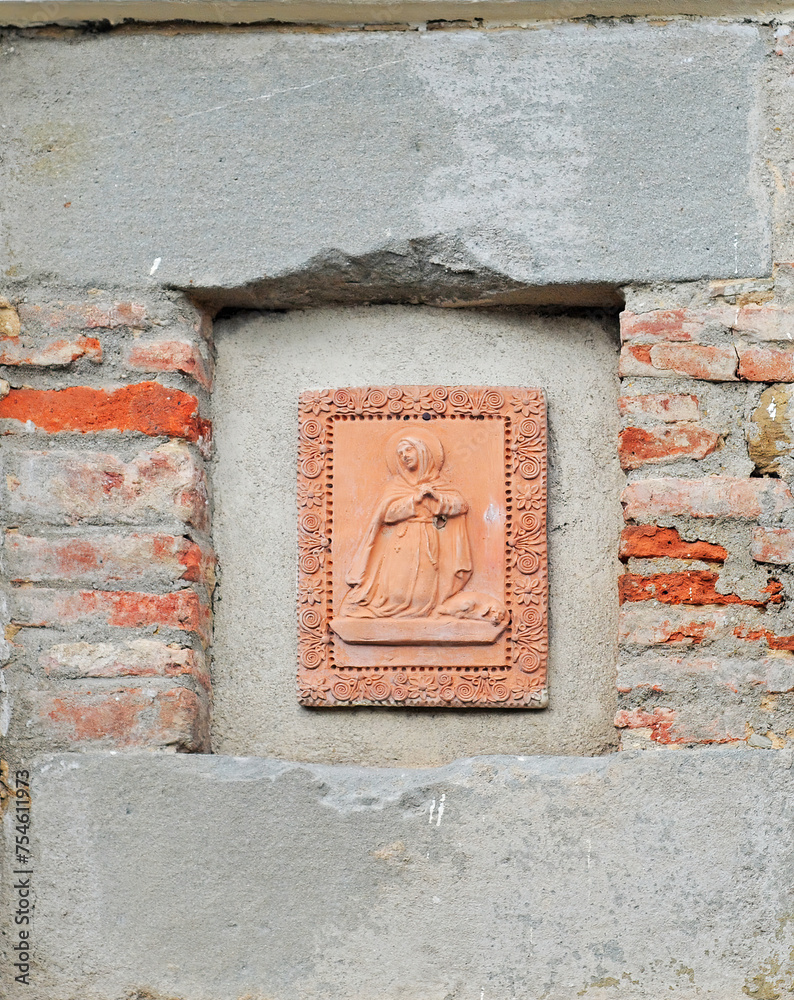 Very old terracotta bas-relief picturing a woman and a dog on a street wall in Cortona, Tuscany, Italy