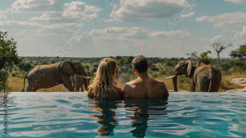  A couple of men and women in a swimming pool with the background Elephants in the savanna in Africa, a safari camp, and a luxury lodge pool in the bush in Africa photo