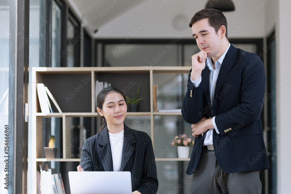 Photo of two business people using laptop computer and working together in the office desk.