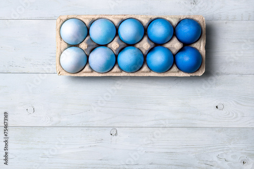 Easter concept. Ombre eggs in blue colors in cardboard packaging on neutral wooden background with copy space for text. Top down view or flat lay