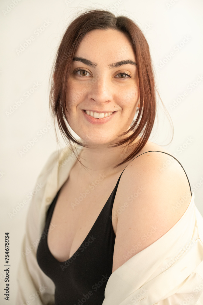 Young brunette womain in black tank top poses befoe a white wall in soft light Young brunette womain in black tank top poses befoe a white wall in soft light