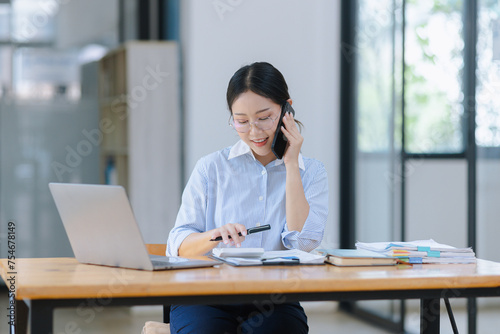 Asian accounting woman using smartphone working with document paper and laptop computer at table office, Financial and accounting woman concept. 