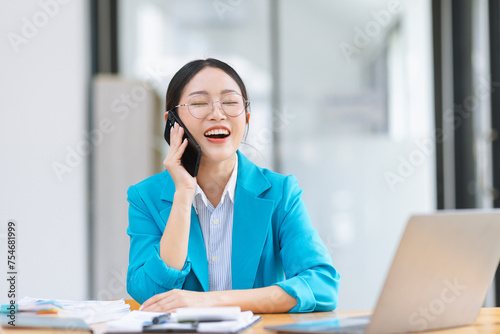 Asian businesswoman wearing a suit using smartphone with digital laptop computer working at modern office, Asian beautiful businesswoman in red suit working in the modern office.