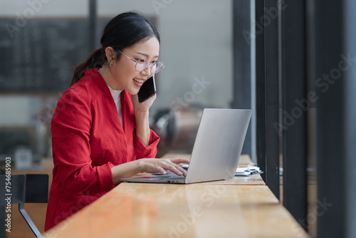Asian businesswoman wearing a suit using smartphone with digital laptop computer working at modern office, Asian beautiful businesswoman in red suit working in the modern office.