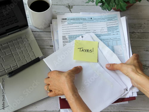 Workspace overhead view of woman getting tax documents ready to file her tax return with laptop, tax forms and coffee cup on her desk.