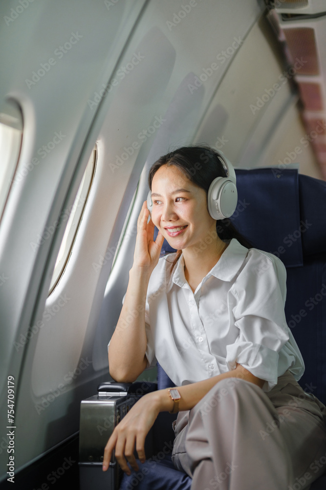 Asian woman sitting and using a smartphone in an airplane Listening to music next to the airplane seat window travel and technology concept Asian woman sitting and using a smartphone in an airplane Listening to music next to the airplane seat window travel and technology concept